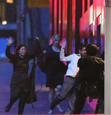 Escaped hostages run with their hands up from the Lindt Cafe during the siege.