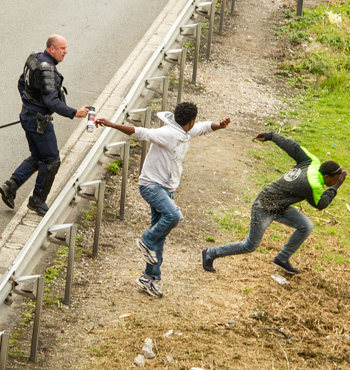 A police officer sprays tear gas onto migrants trying to access the Channel Tunnel in Calais.