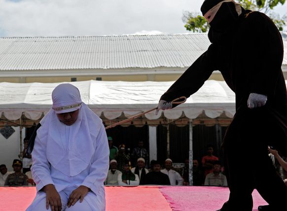Sharia law officers in Indonesia punish a woman accused of cheating on her husband by whipping her on stage in public this month. Photo: Getty.