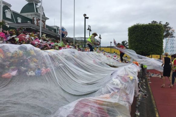 Dreamworld staff and Red Cross volunteers cover the floral memorial outside the park to protect it from rain.