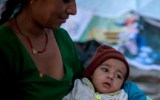 A woman holds a child as she sits in the open area because of the disincentive for an after shock following a second major earthquake