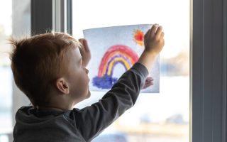 Young Boy sticking his drawing on home window during the Covid-19 crisis - stock photo