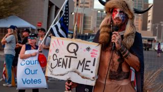 Jake Angeli, known as the "QAnon Shaman," holds a sign reading "Q Sent Me" as supporters of US President Donald Trump gather to protest