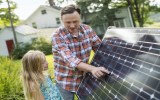 A man and a young girl looking at a solar panel in a garden.