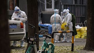 Workers wearing personal protective equipment (PPE) are seen by the entrance to a residential area under lockdown in Beijing